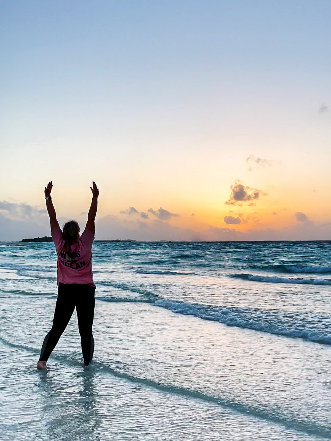 woman with feet in the ocean and hands up, happy after controlling her gout