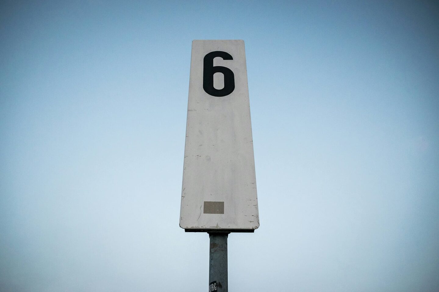 Tall skinny white street sign with the number 6, representing the gout uric acid level target of 6.0 mg/dL