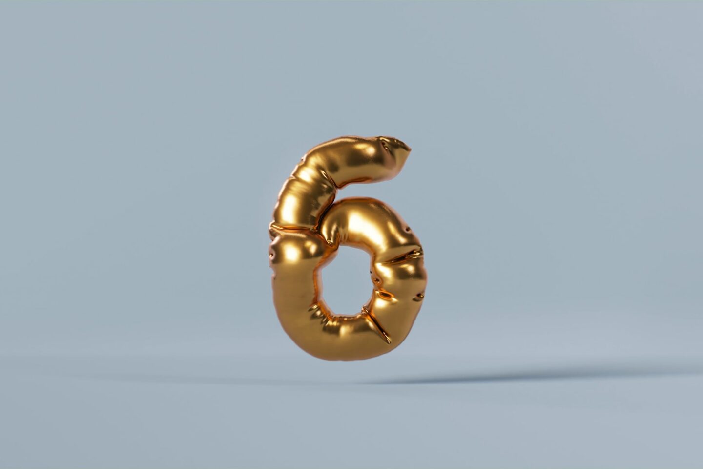 gold foil balloon of the number 6 floating on a blue background, representing the target gout uric acid level of 6.0 mg/dL