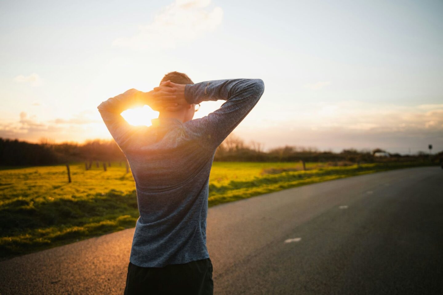 Man with hands up behind head looking down a road considering the path ahead