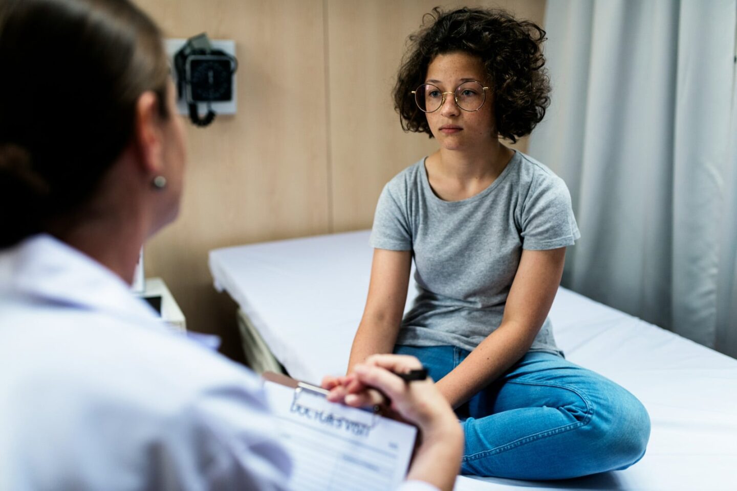 woman in an urgent care sitting on a bed looking depressed, speaking with her doctor about gout
